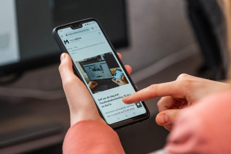 vrouw die op gsm scrollt met een blogpost geschreven door externe marketingbureau maesmedia
